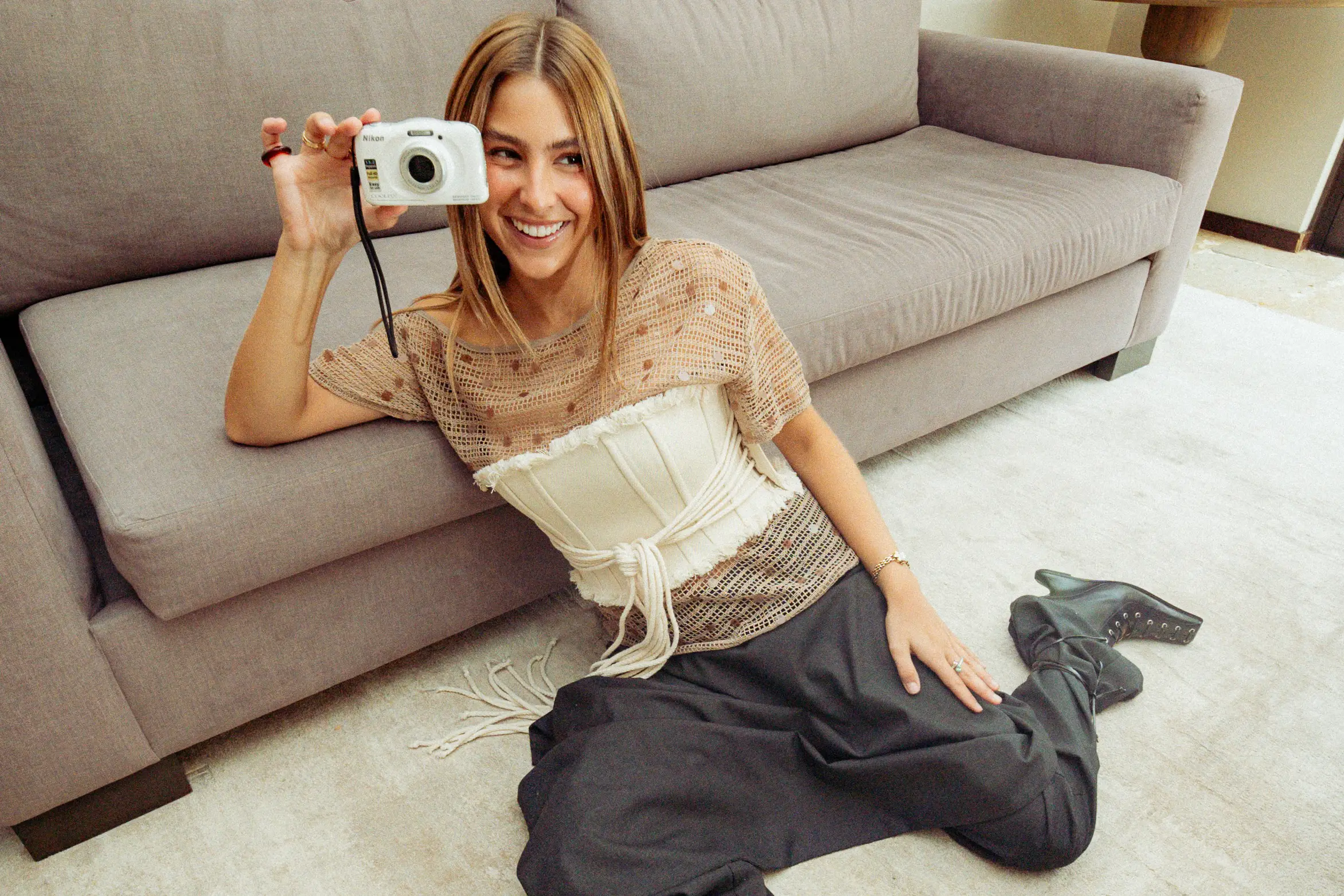 Maca sentada en el piso junto al sillón, sonriendo detrás de una cámara blanca