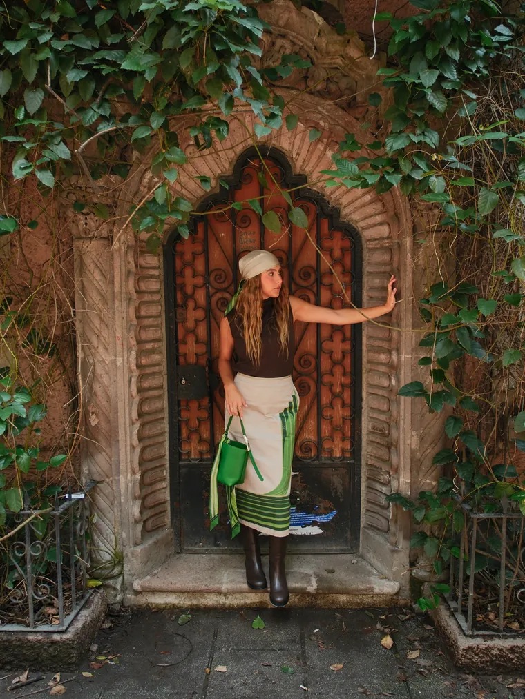 Maca en una puerta con hiedra, con una bolsa verde de Longchamp