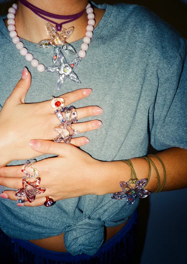 Manos con anillos y collares de flores de colores de Vold