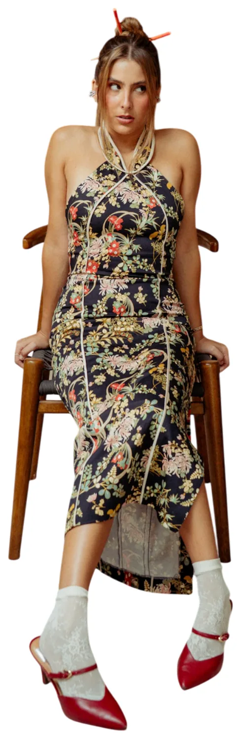 Macarena Olávarri sentada en una silla de madera, con vestido de flores, calcetas de encaje y zapatos rojos